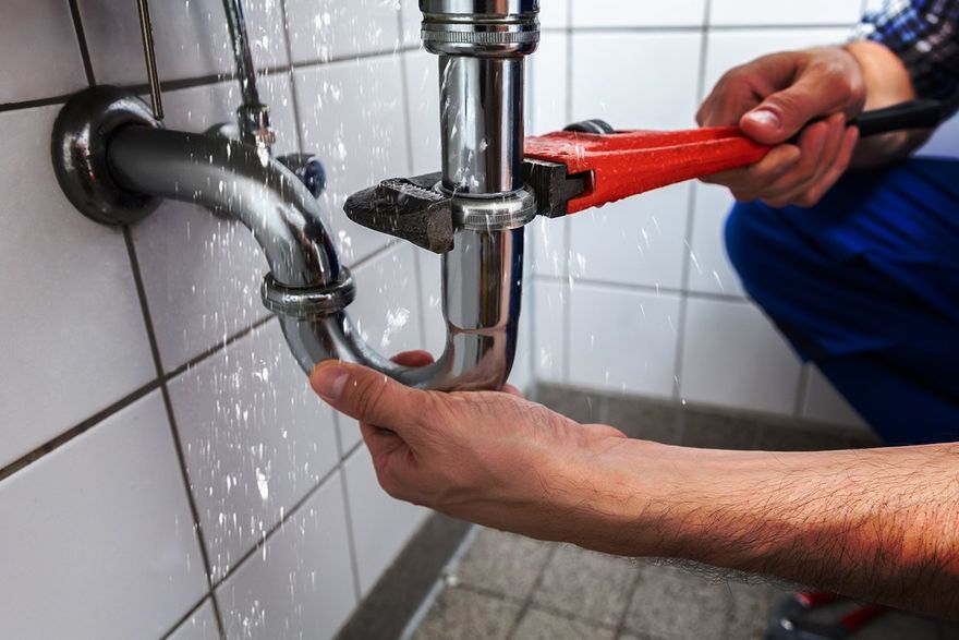 A plumber is fixing a leaking pipe in a bathroom with a wrench.
