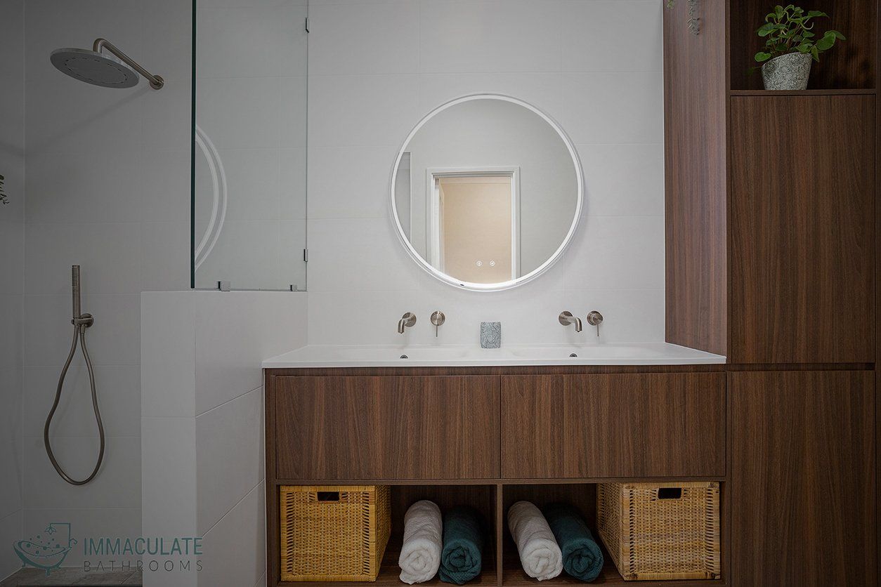 A bathroom with two sinks , a round mirror , and wicker baskets.
