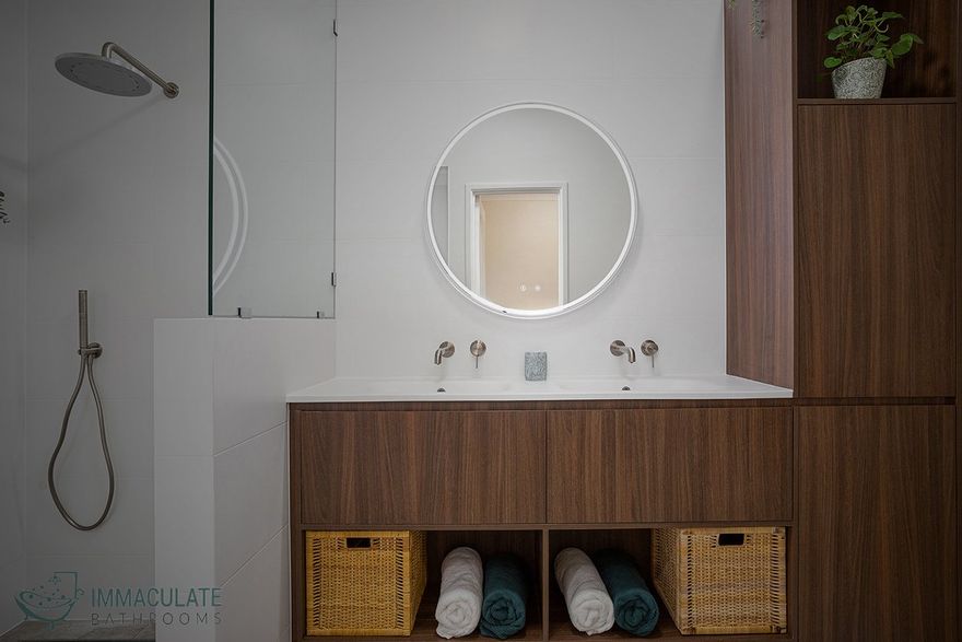 A bathroom with two sinks , a round mirror , and wicker baskets.