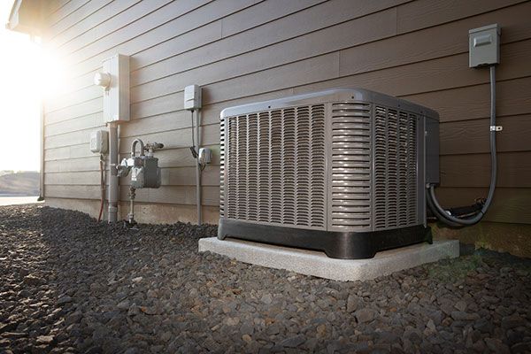 Air conditioning unit outside a brown house, gravel ground, sunny day.