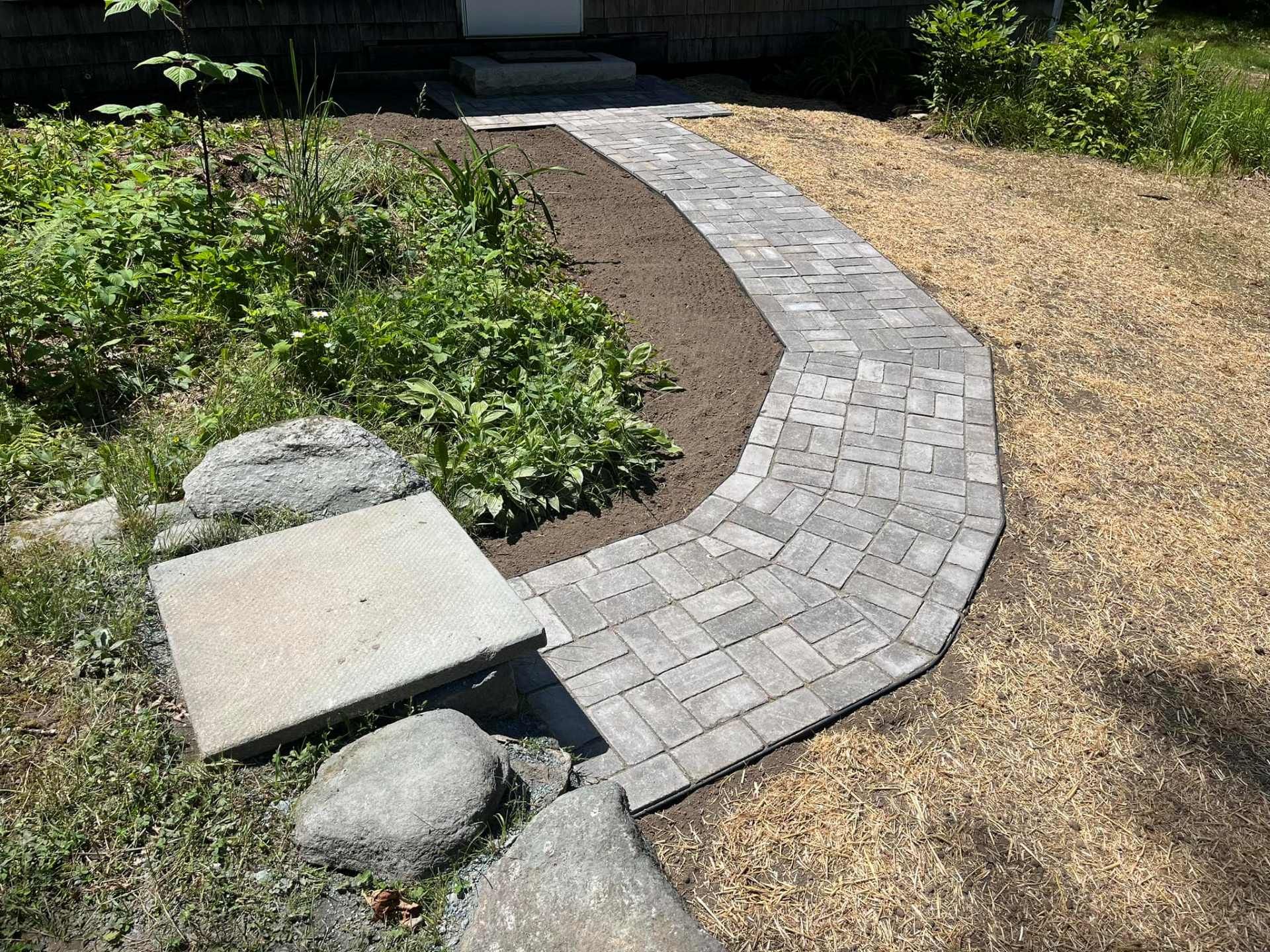Brick pathway leading to a house, surrounded by plants and grass.