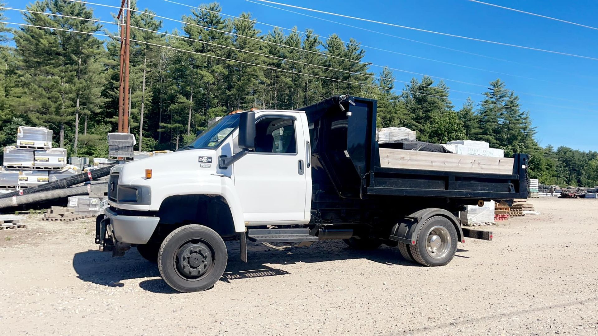 White dump truck parked outdoors, loaded with materials, trees in background, sunny day.