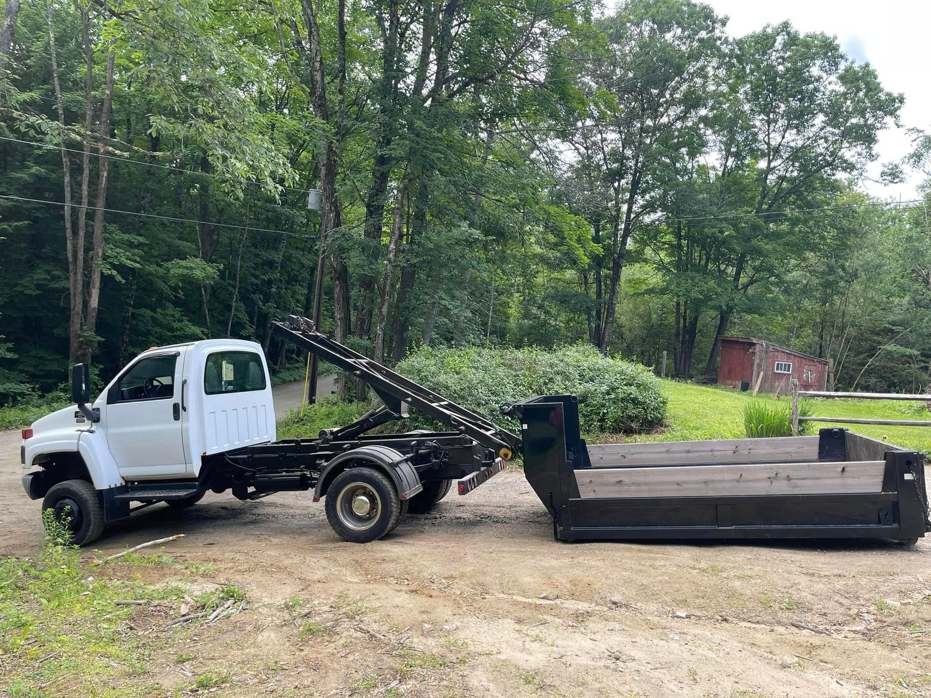 White truck with a black dumpster in a wooded area.