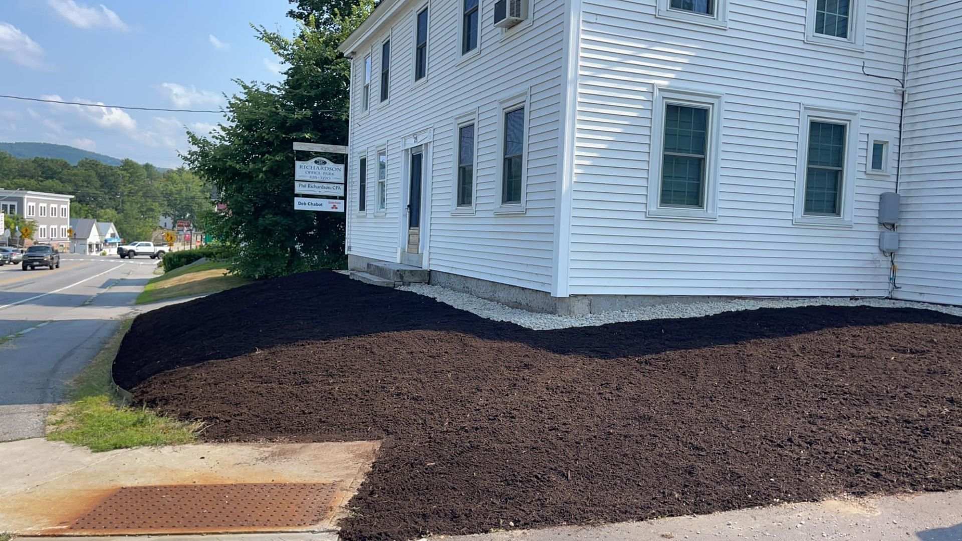 White building with dark mulch landscaping beside a street.