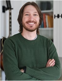 Smiling person in a green sweater with arms crossed in a bright room