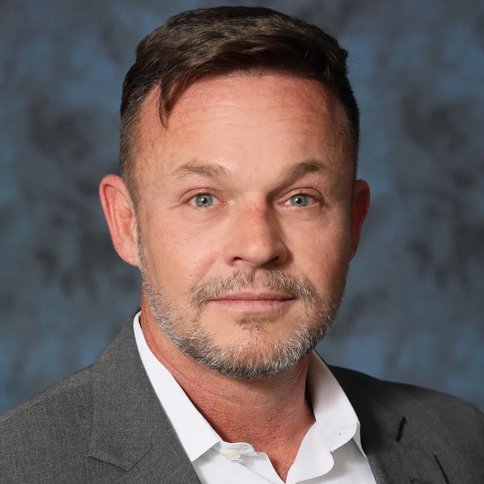 Portrait of a man in a gray suit and white shirt against a mottled blue-gray background