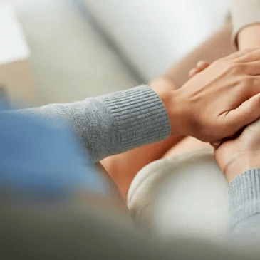 Hands gently clasped in a comforting gesture over a gray sweater sleeve
