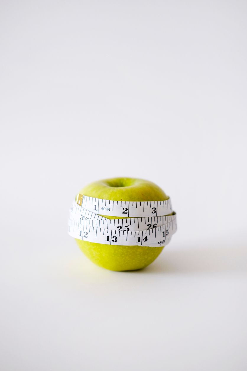 Green apple wrapped with a white measuring tape on a white background