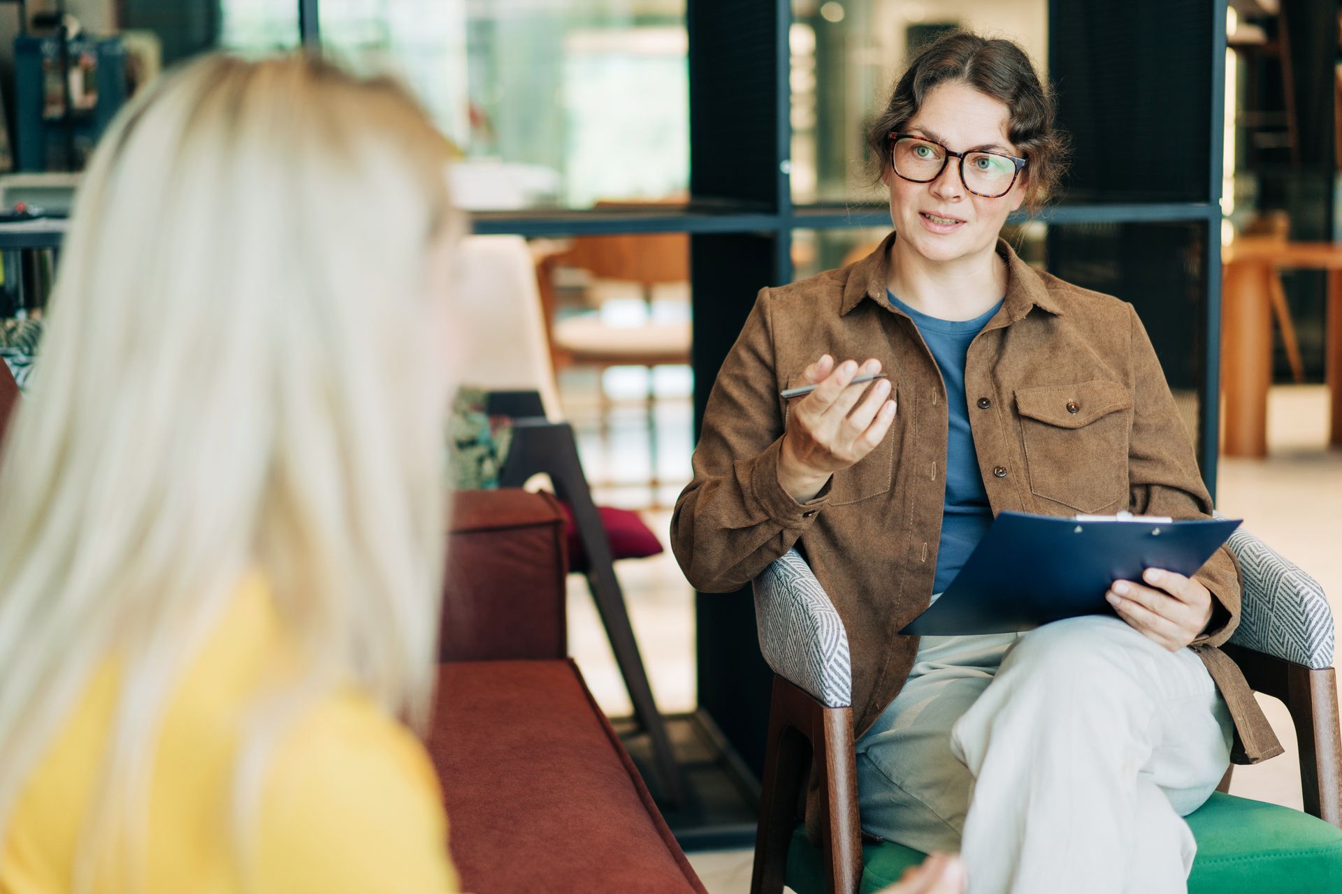Two people in a café, one holding a clipboard and gesturing during a conversation
