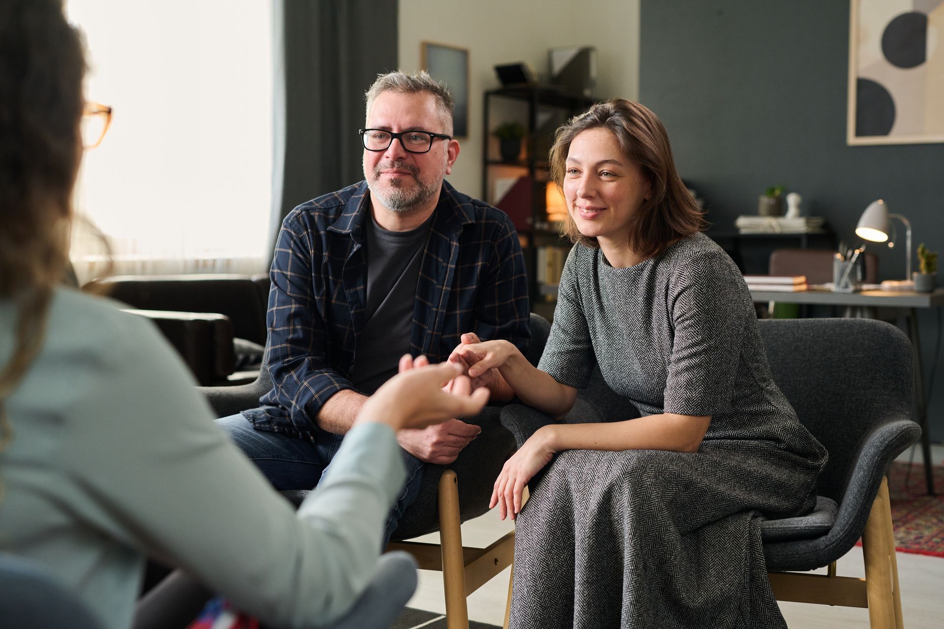 Two people smiling and talking with a therapist in a cozy office setting