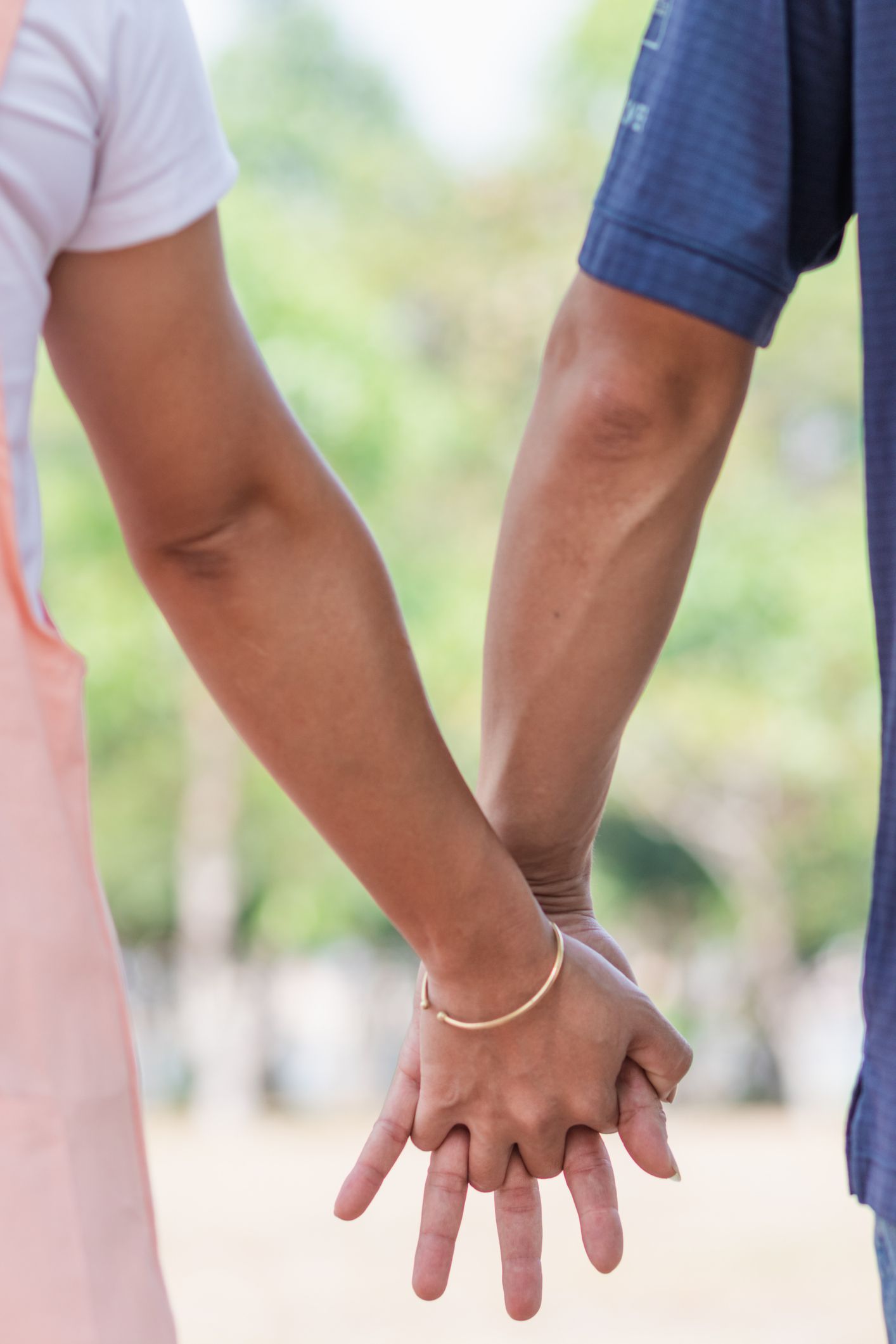Two people holding hands outdoors, one in a white shirt and one in a blue shirt.