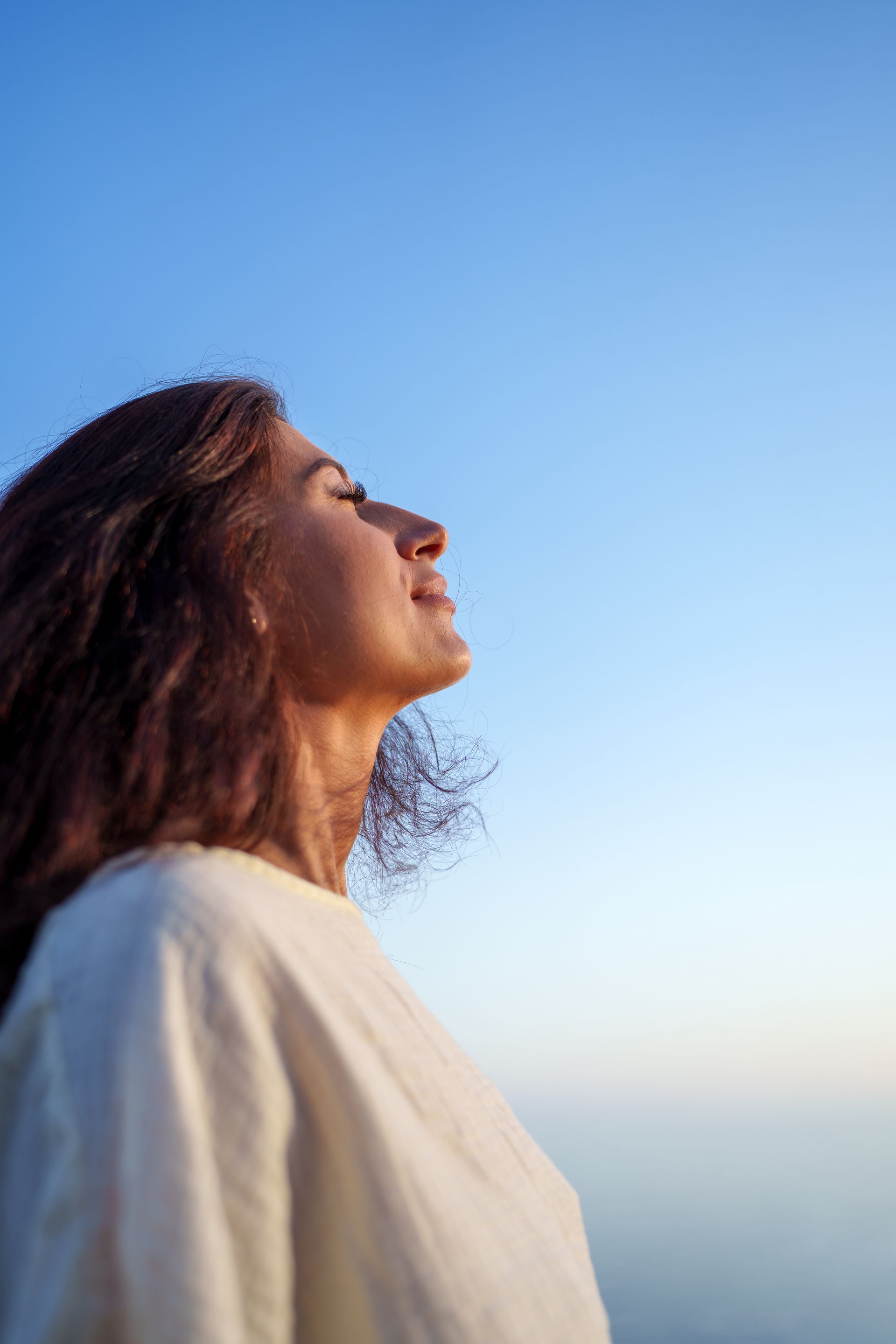 Person in a white shirt looking up against a clear blue sky.