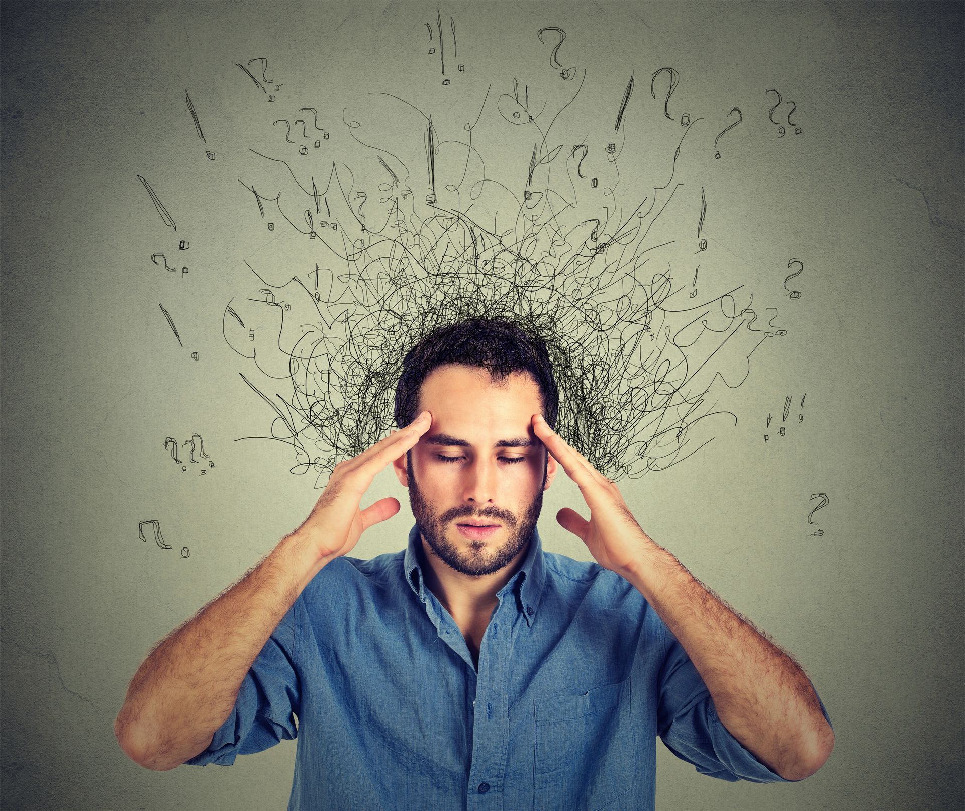 Stressed man holding temples as scribbled lines burst from his head on a gray background