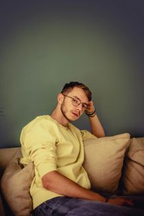 Person in a yellow shirt lounging on a couch, resting against a beige pillow.