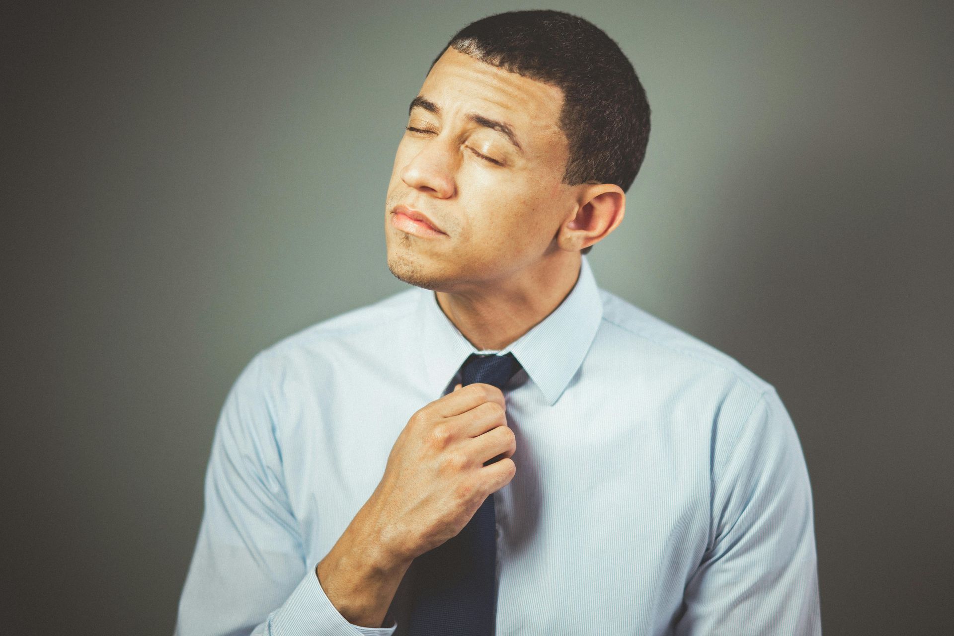 Man adjusting his tie with eyes closed against a gray background