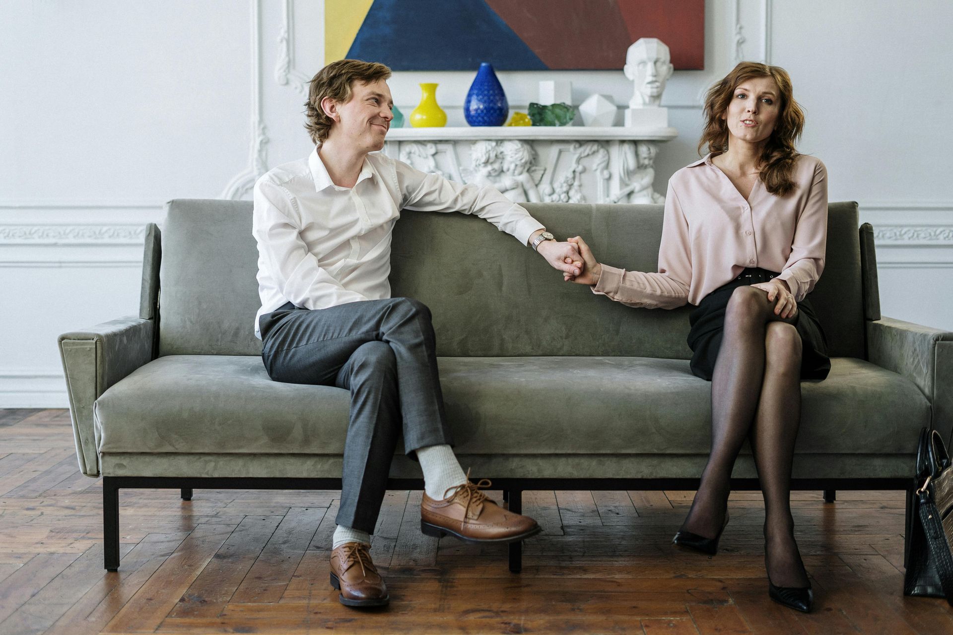 Two people sitting on a green sofa, holding hands in a bright living room
