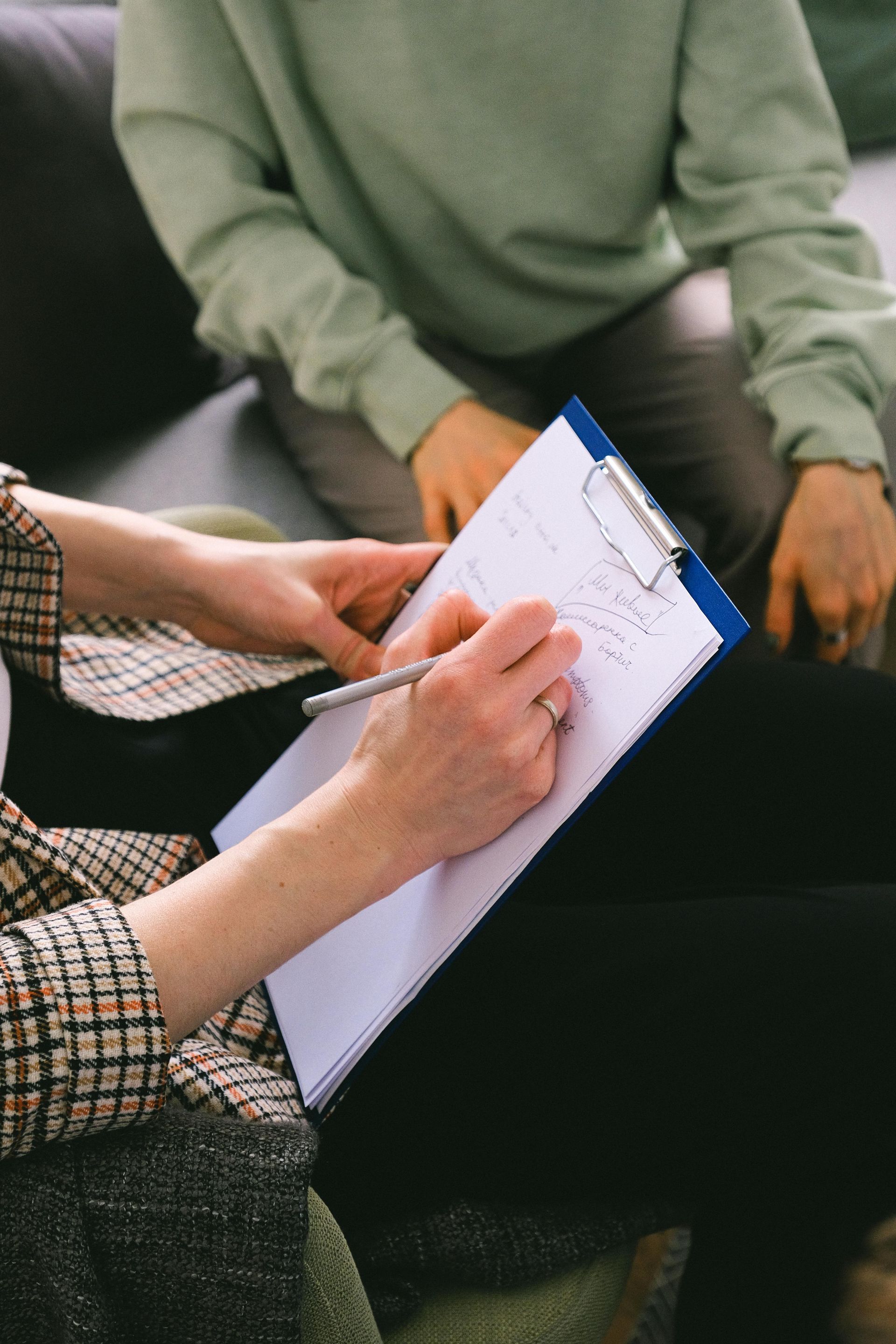 Hands writing on a clipboard during a seated meeting
