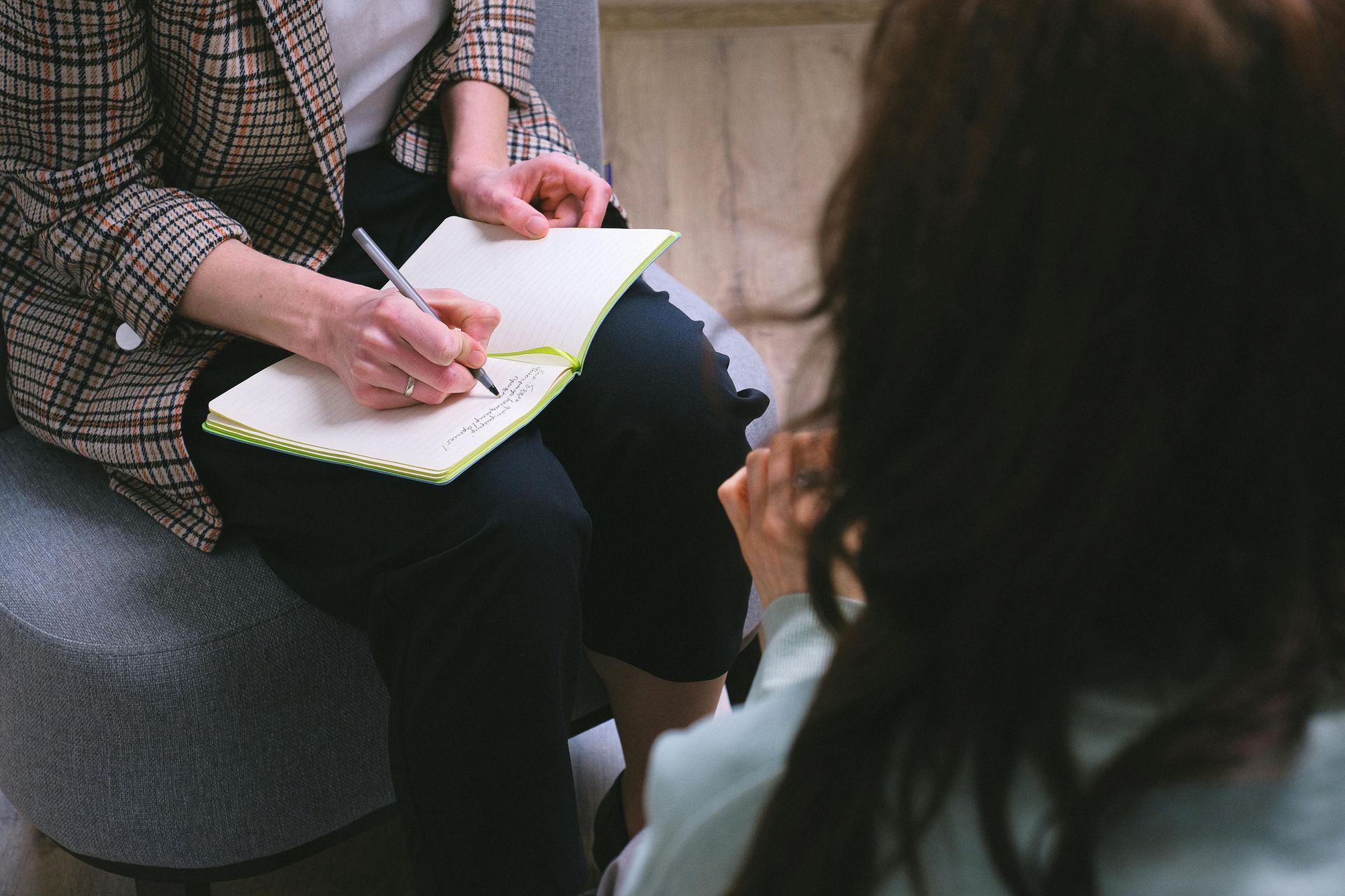 Person writing in a notebook while seated across from another person in a consultation setting