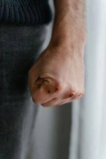 Clenched fist of a person wearing a dark shirt against a blurred gray background