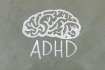 Chalk drawing of a brain above the word “ADHD” on a gray background