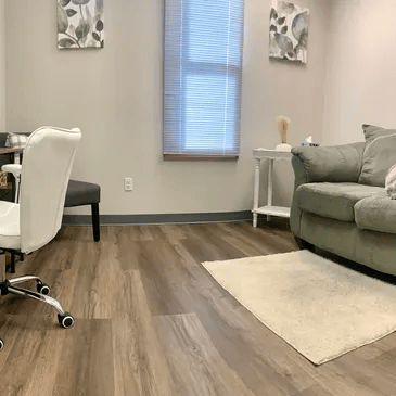 Modern living room with gray sofa, white desk chair, wood flooring, and a beige rug
