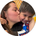 Close-up of a person kissing a smiling child on the cheek while holding a colorful snack container