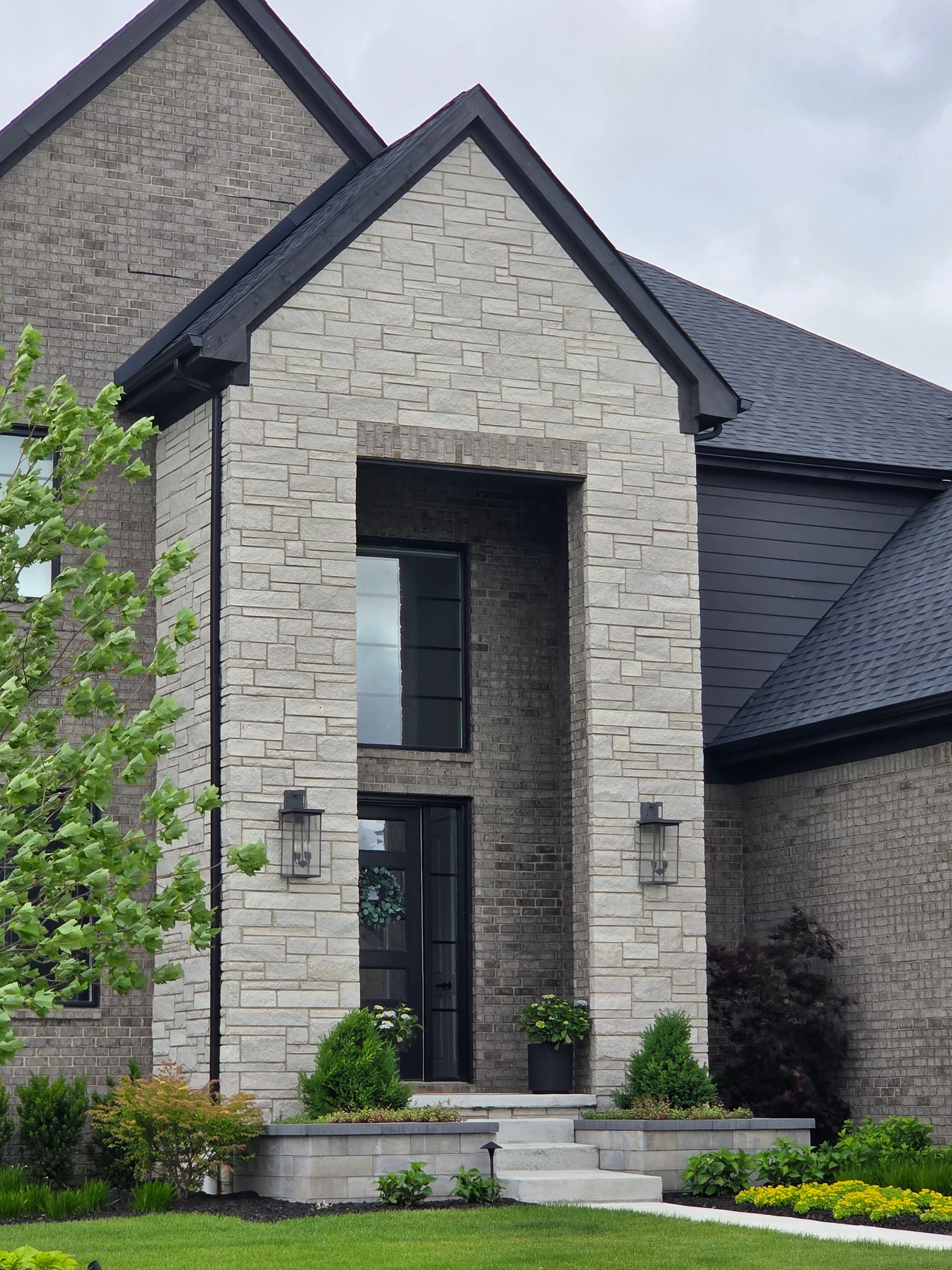 Modern stone house entrance with tall doorway, black roof, and landscaped front steps