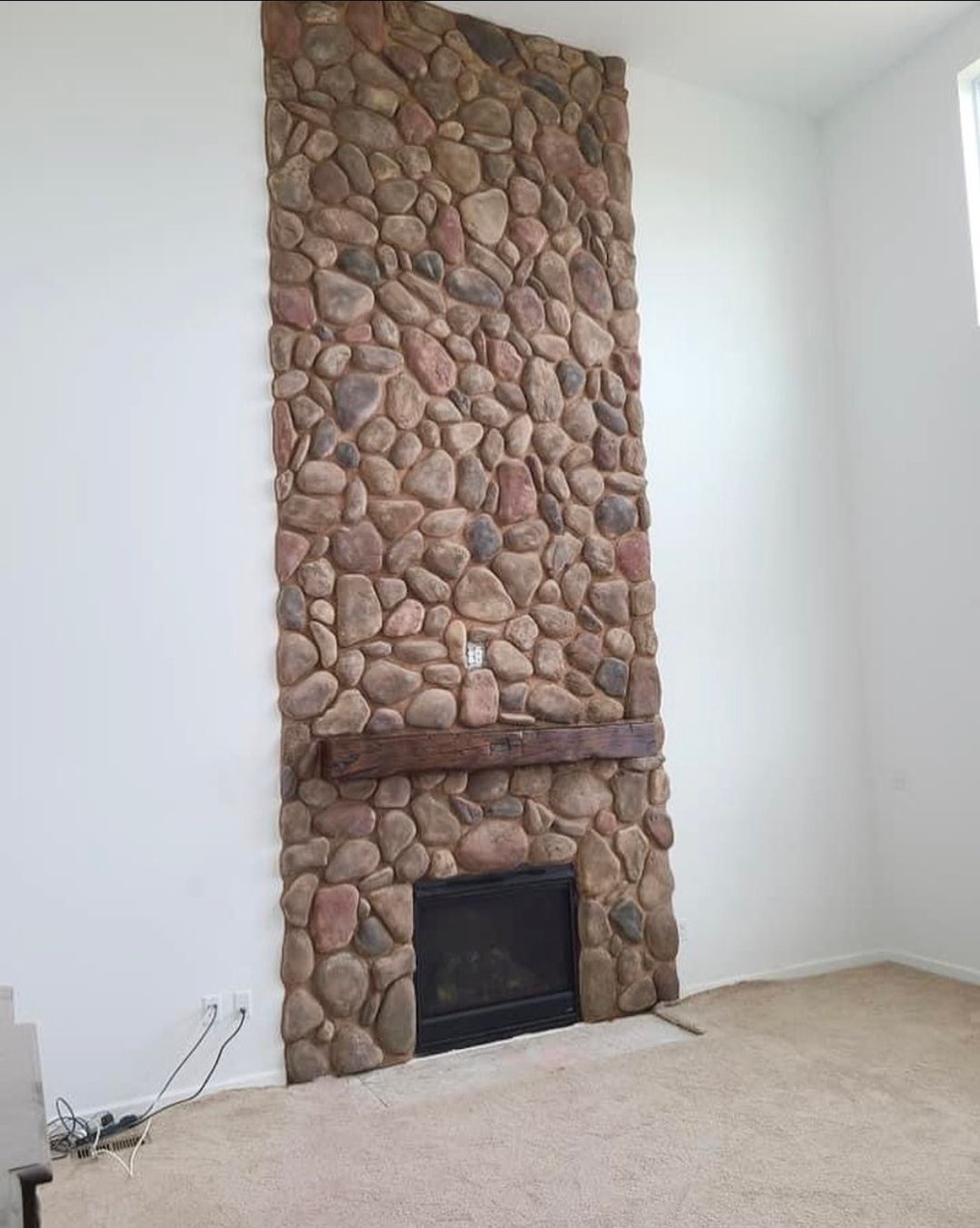 Stone fireplace with black firebox in a white room with beige carpet