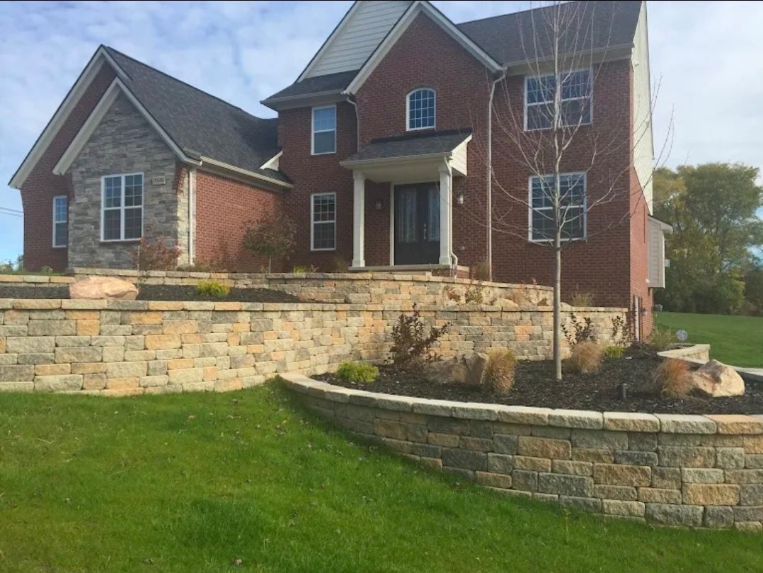 Large brick house with stone retaining walls and green lawn on a sunny day