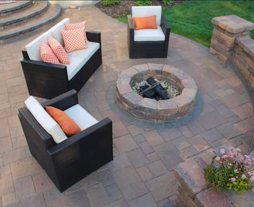 Outdoor patio with three black armchairs around a circular fire pit on a stone paver terrace