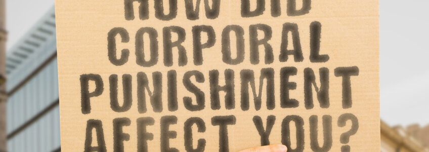A cardboard sign held up outdoors with the black, stenciled text: