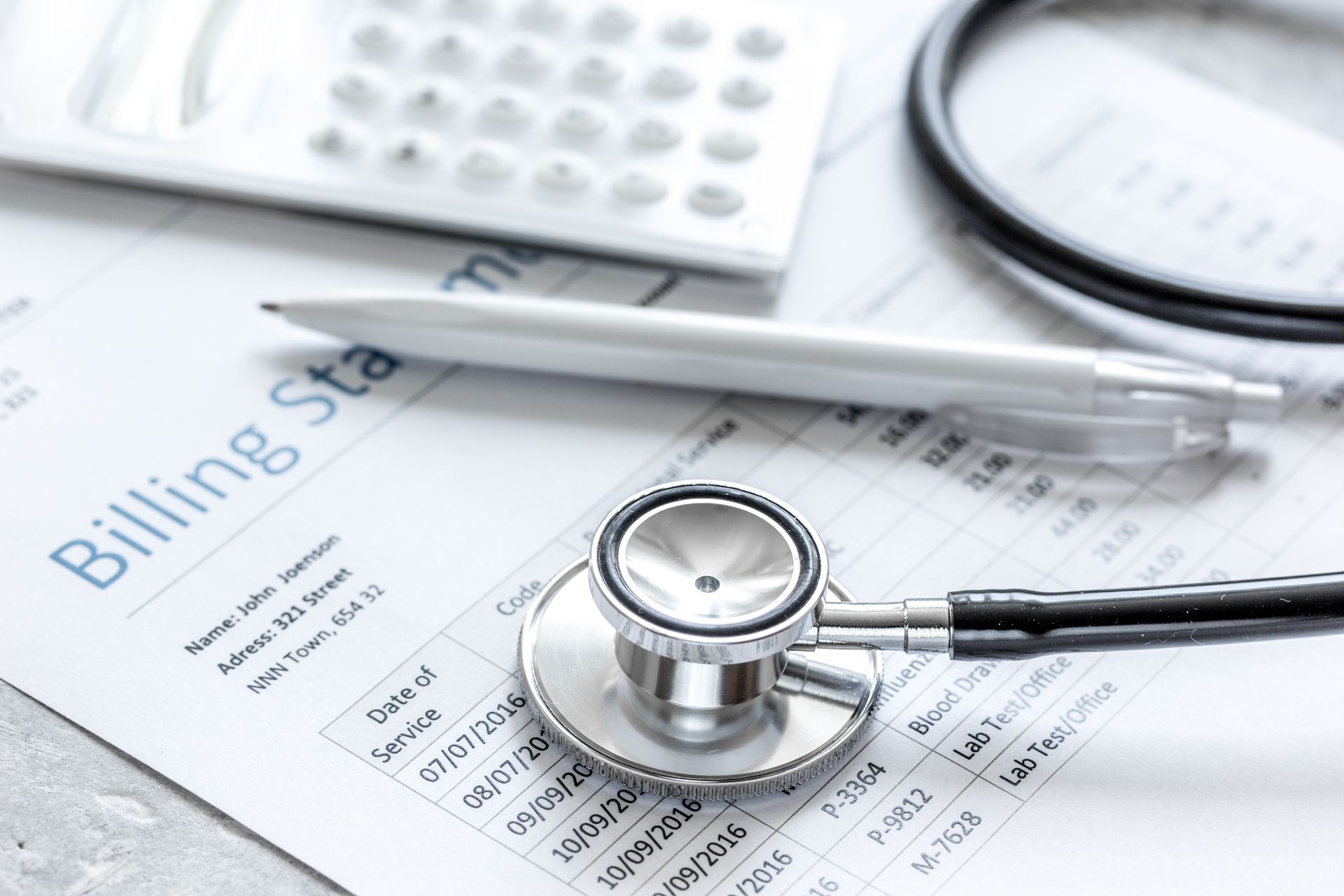 A stethoscope and a silver pen rest on a medical billing statement next to a calculator.