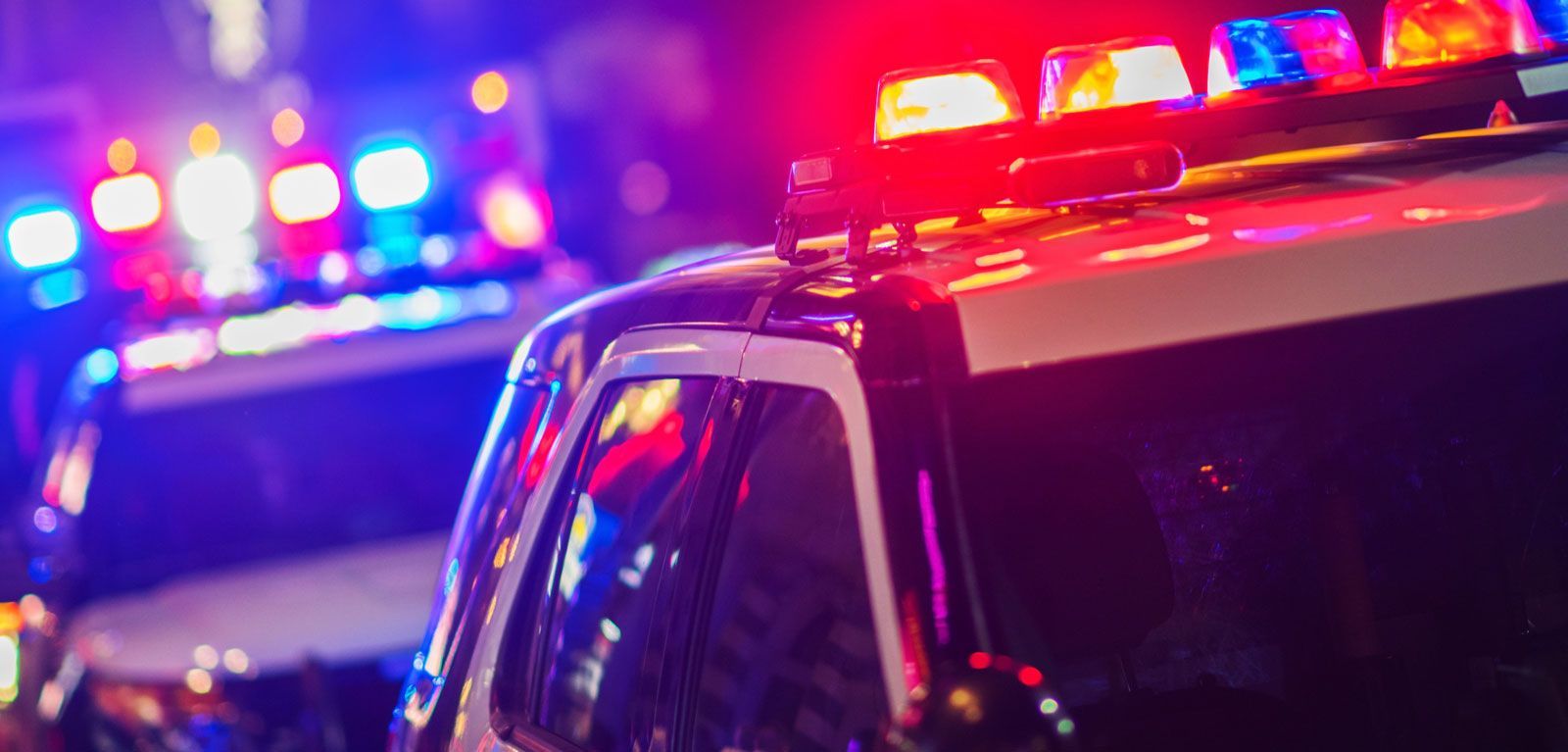Two police vehicles at night, illuminated by bright, flashing red and blue emergency lights.