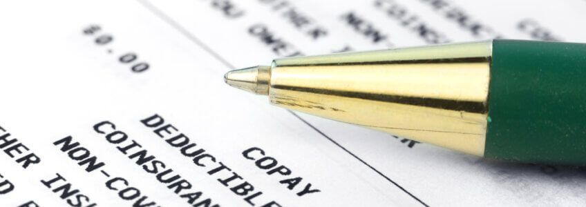 A green pen rests on a document displaying medical billing terms like copay, deductible, and coinsurance.