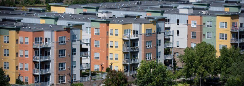 A row of modern, multi-story apartment buildings in shades of yellow, orange, and gray with balconies.