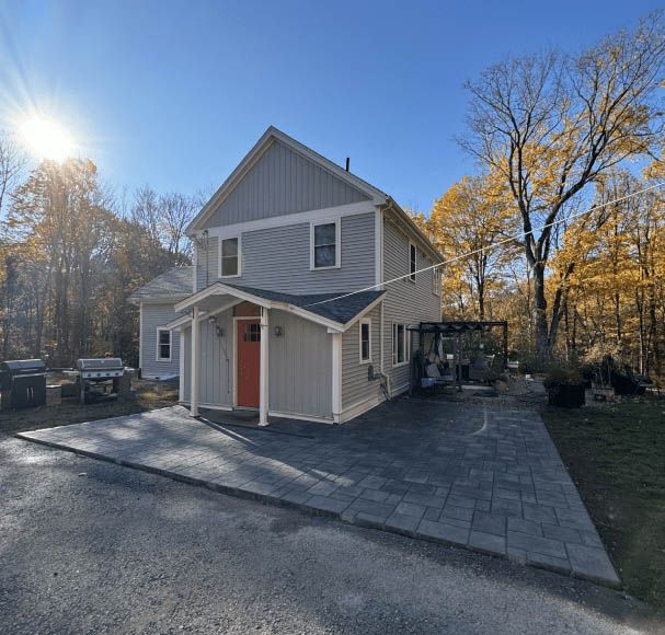 A small house with a red door is surrounded by trees on a sunny day.