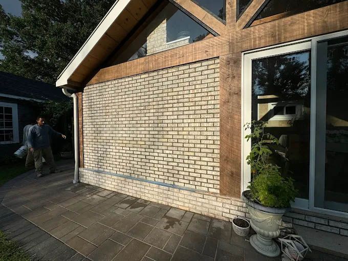 A man is standing in front of a house with a brick wall.