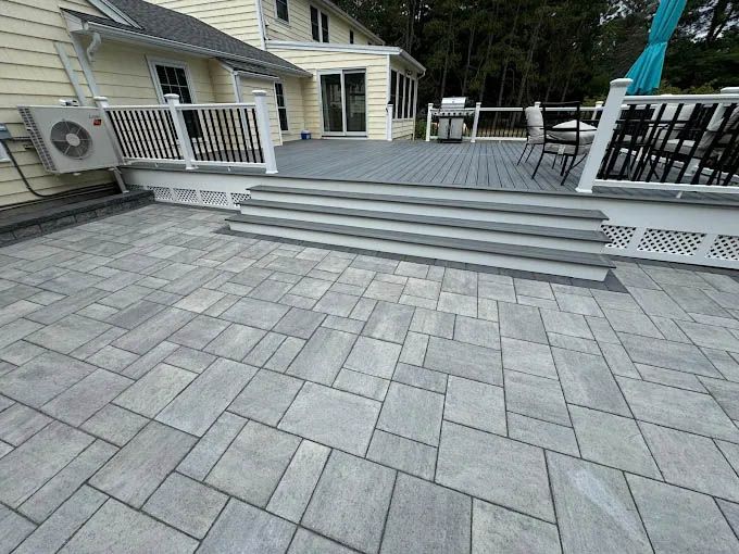 A patio with a deck and stairs in front of a house.