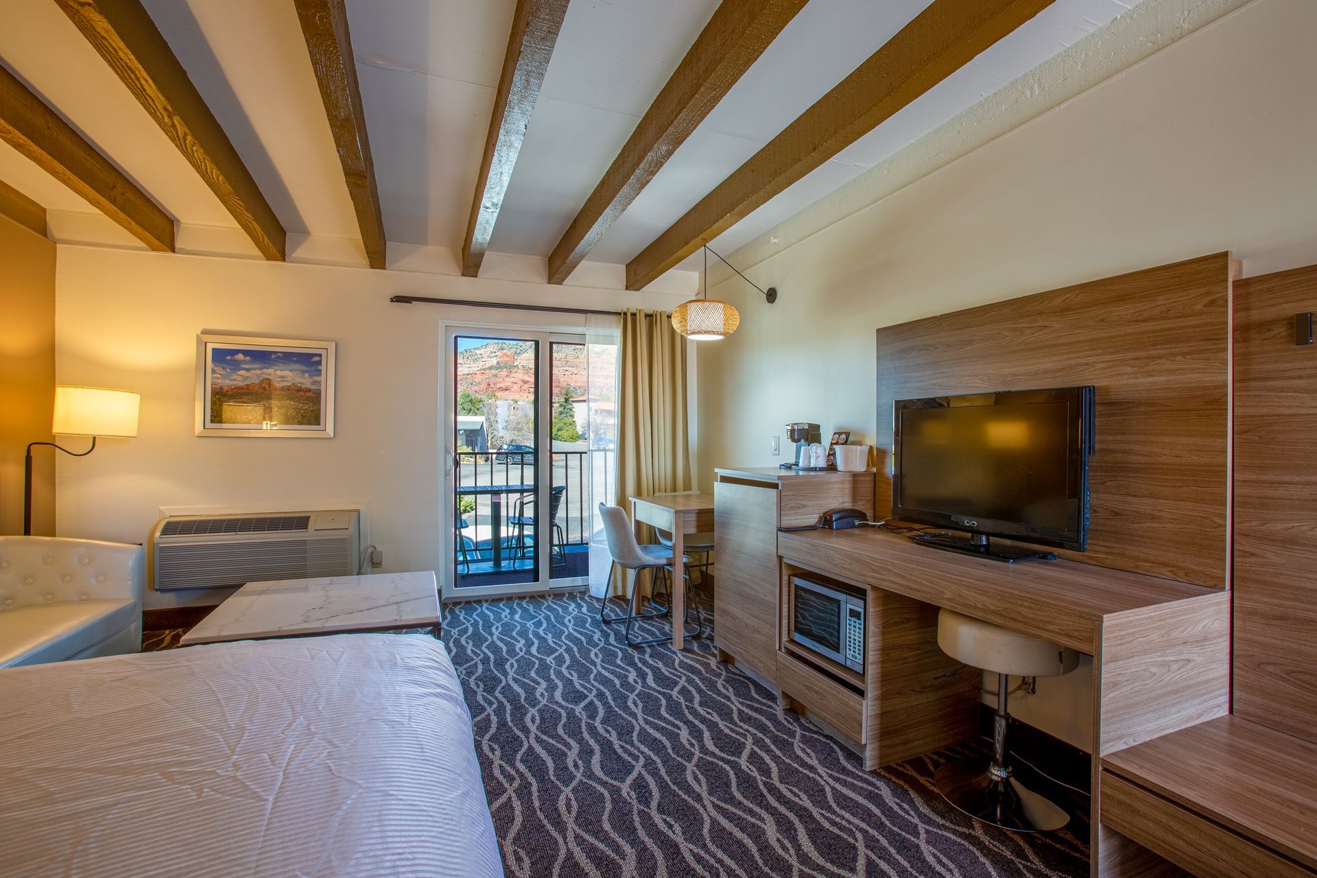 Dreamcatcher Inn Sedona hotel room with bed, work desk, flat-screen TV, and private balcony overlooking Sedona views