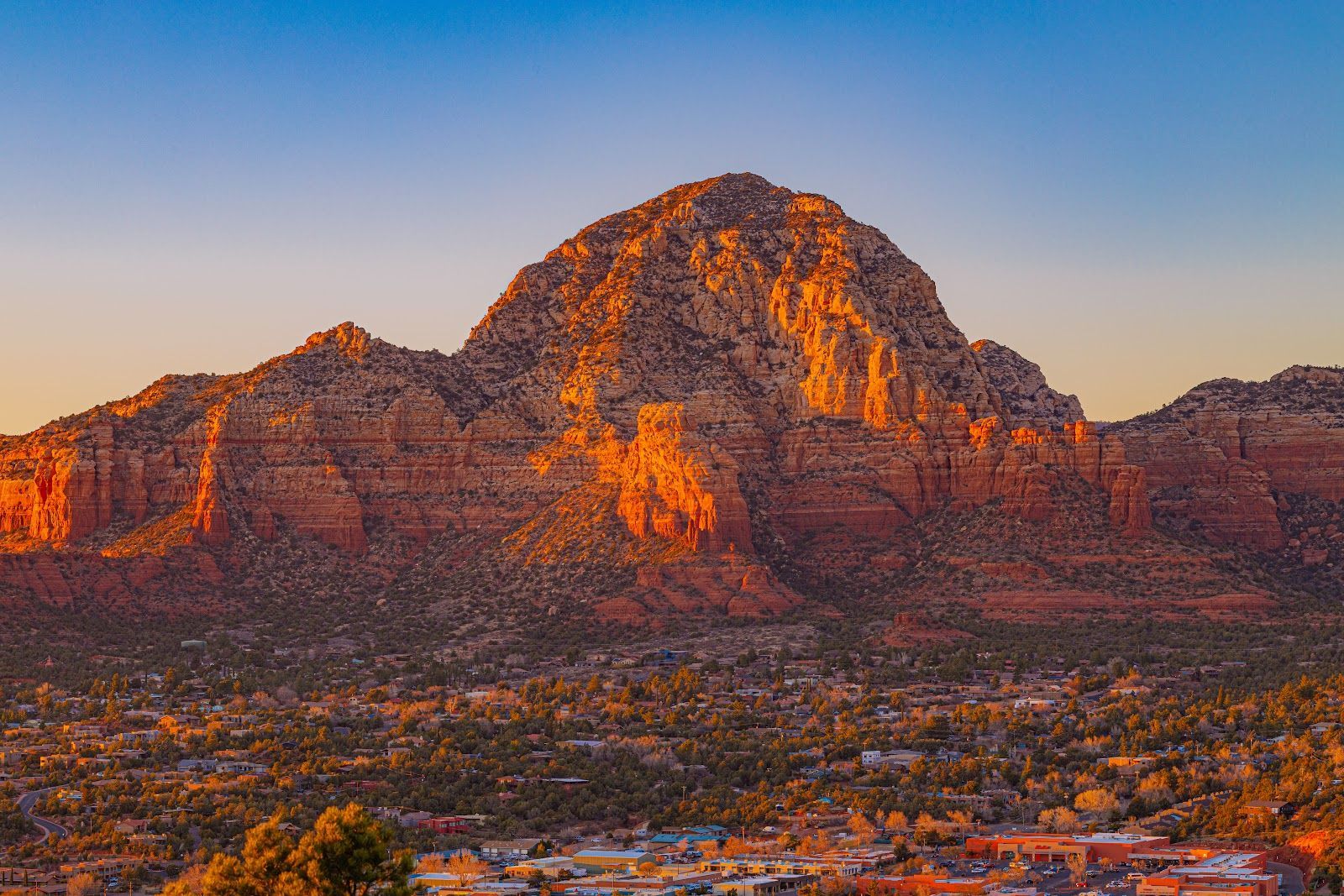Wide view of Sedona's red rock landscape glowing at golden hour above the valley below