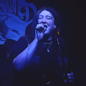 Singer performing onstage under blue lighting, holding a microphone and smiling