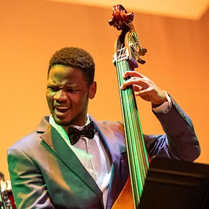 Musician playing upright bass on stage, singing with eyes closed under warm orange lighting
