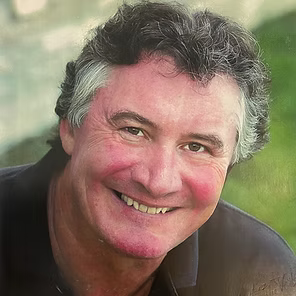 Smiling man with gray hair outdoors against a soft green background