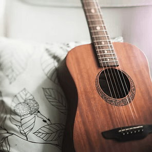 Acoustic guitar resting on a couch with a leaf-patterned pillow