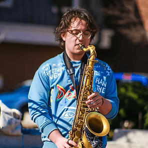 Musician in a blue shirt playing a saxophone outdoors in bright sunlight