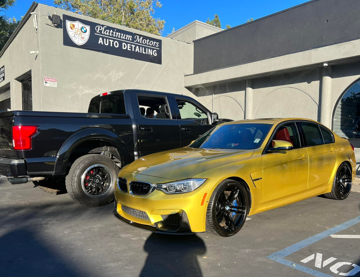 A yellow car is parked next to a black truck in front of a building. | Platinum Motors Martinez