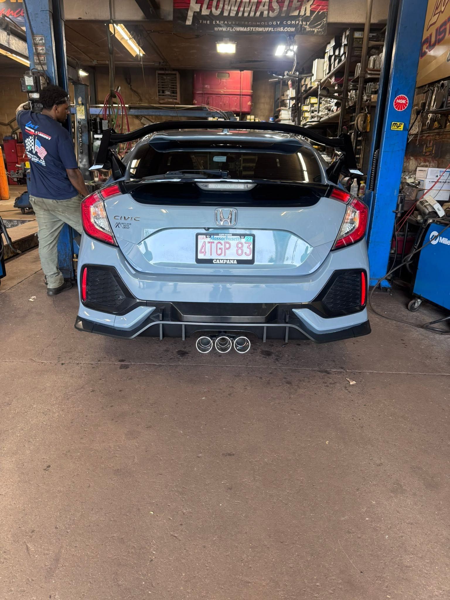 Light blue hatchback in an auto shop with a mechanic nearby and tools around it