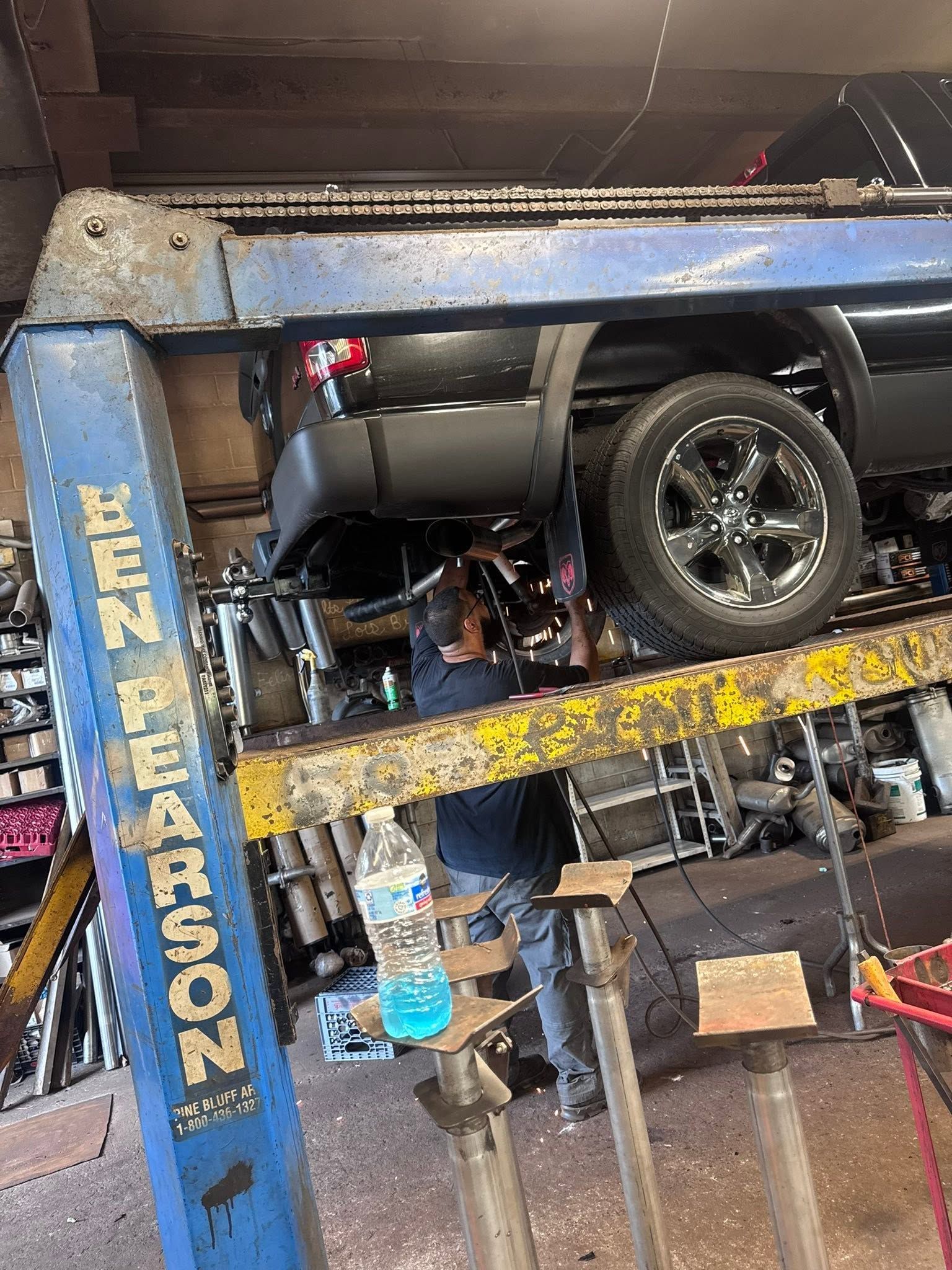Car on a vehicle lift in an auto repair shop with a blue mechanic’s lift and tools below.