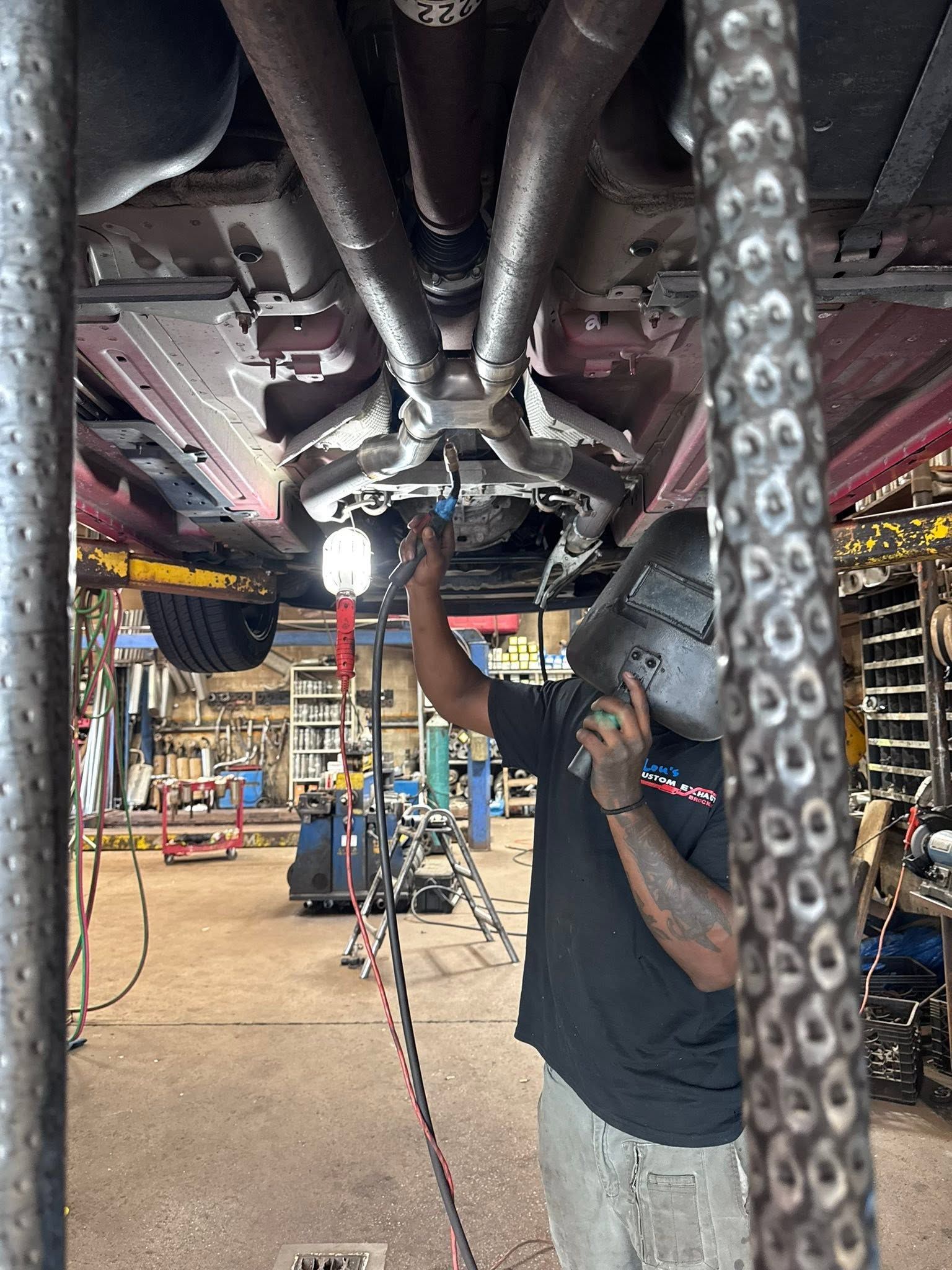 Mechanic working under a car in a garage, inspecting the underside with tools nearby.