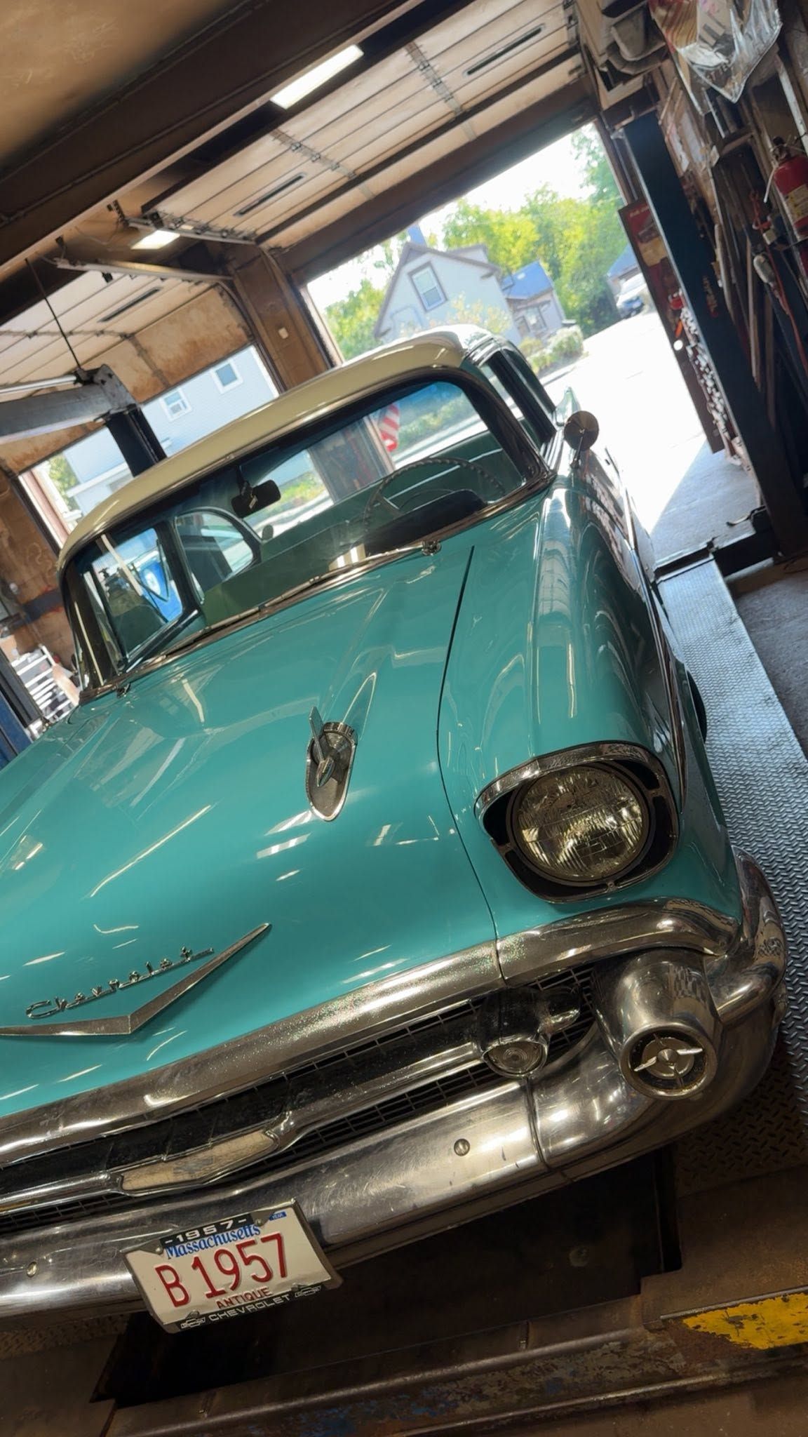 Turquoise vintage car parked inside a garage, viewed from the front at a slight angle.